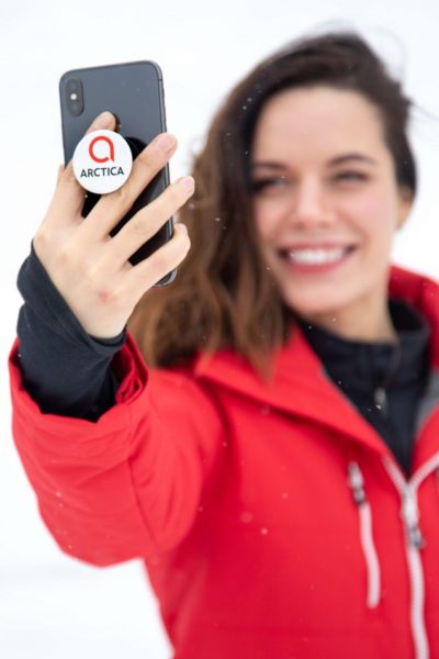 Girl wearing a red Arctica Comp Jacket holding her cell phone with an Arctica PopSocket