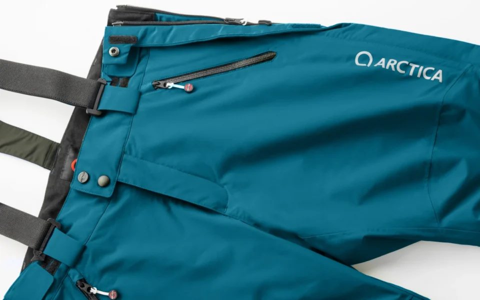 Close-up of the Arctica Side Zip Ski Pants 2.0 in Petrol showing the waistband, suspenders, zip pocket and logo.