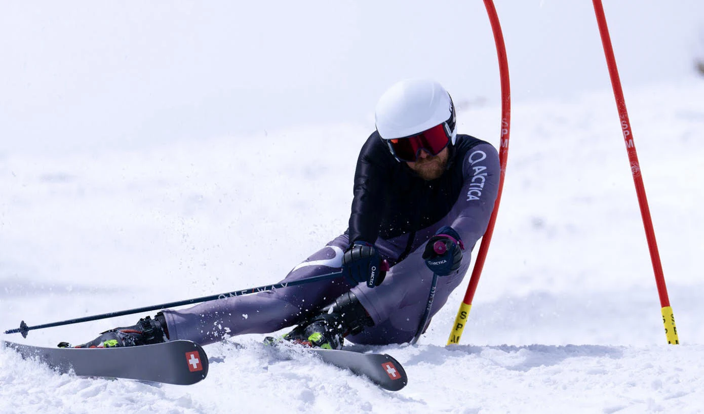 Racer in a gray and black Arctica ski race suit carving past red race gates