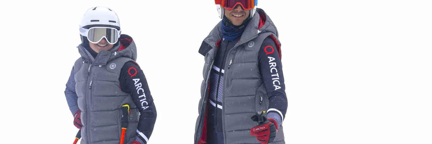 Two smiling skiers wearing grey Arctica down vests over navy Arctica tops