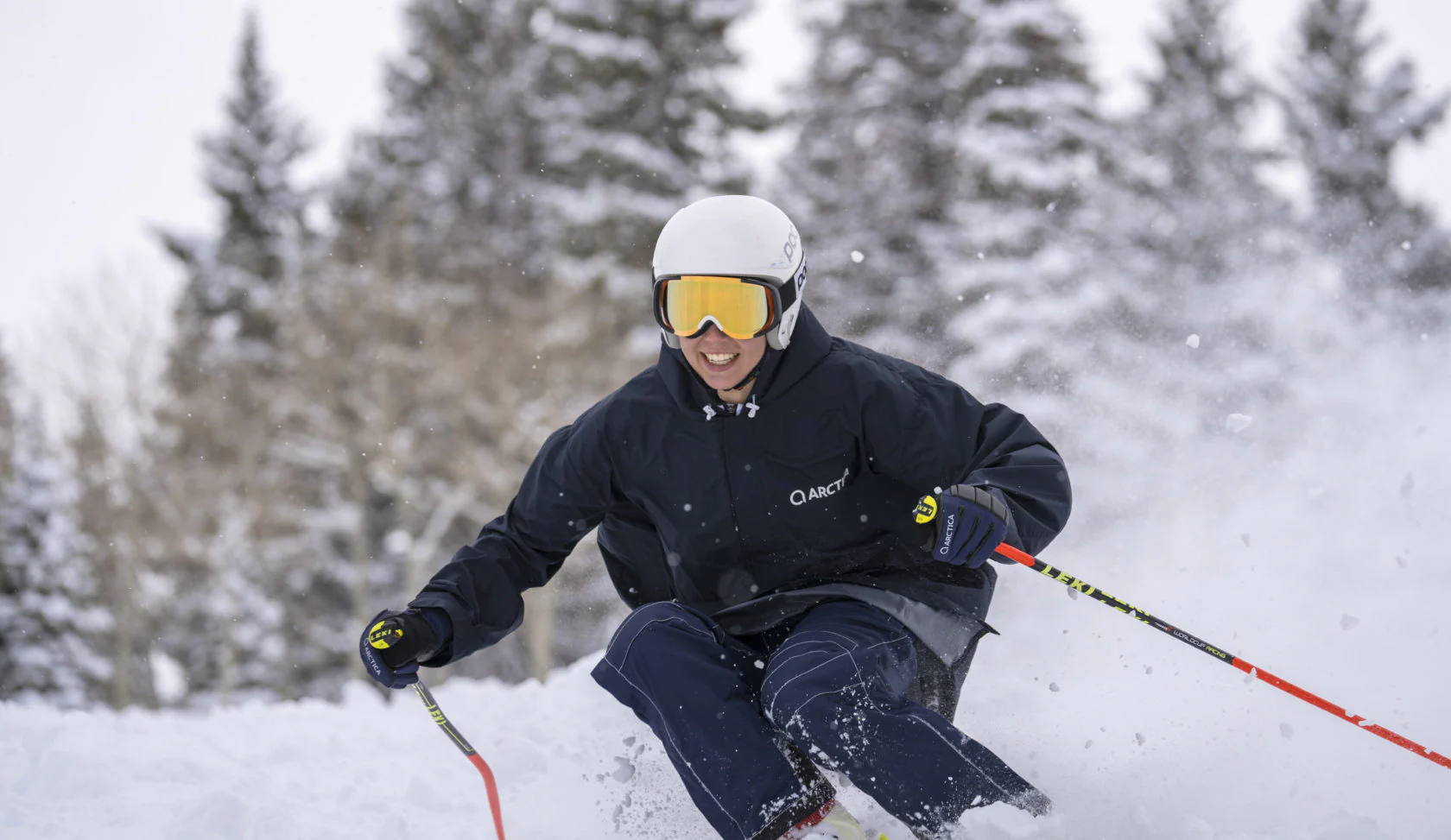 Smiling skier in a navy Arctica jacket and ski pants turning through fresh powder