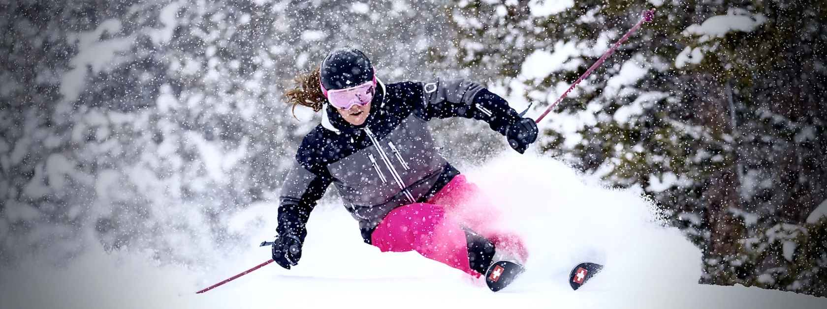 Skier in pink Arctica side zip ski pants and a black and grey jacket carving through powder in falling snow