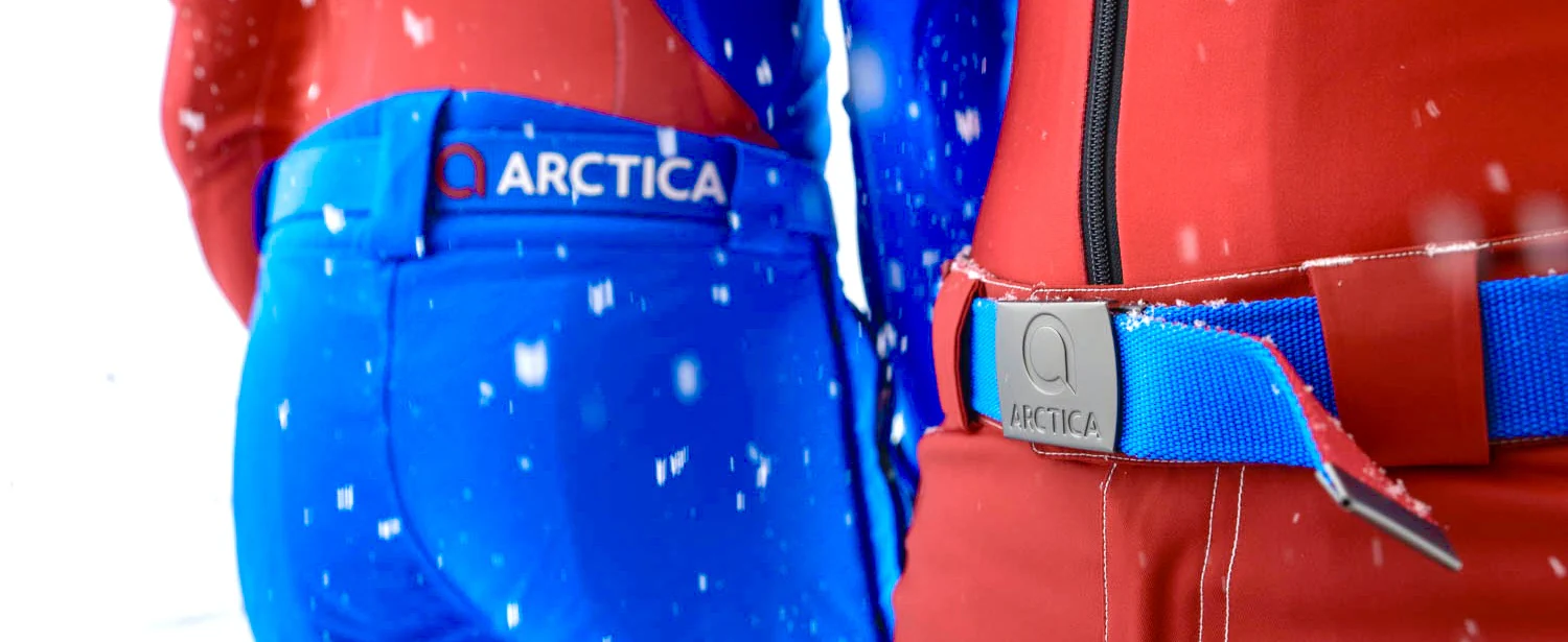 Close-up of blue and red Arctica side zip ski pants with a logo waistband and a blue belt with an Arctica buckle