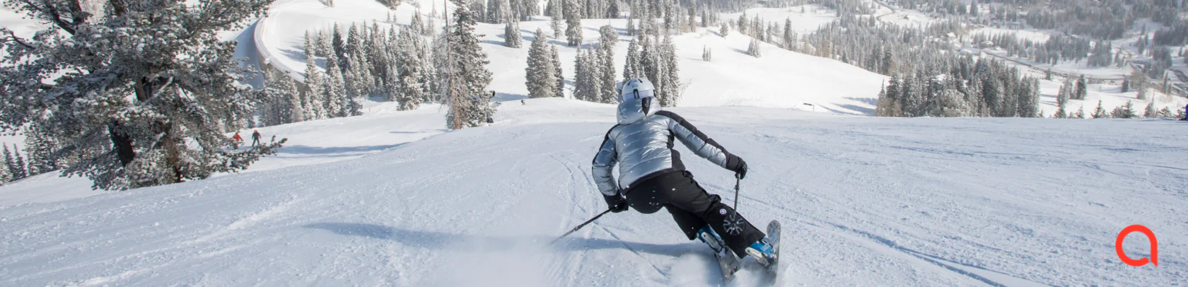 Skier in a silver Arctica down jacket and black ski pants carving down a groomed slope