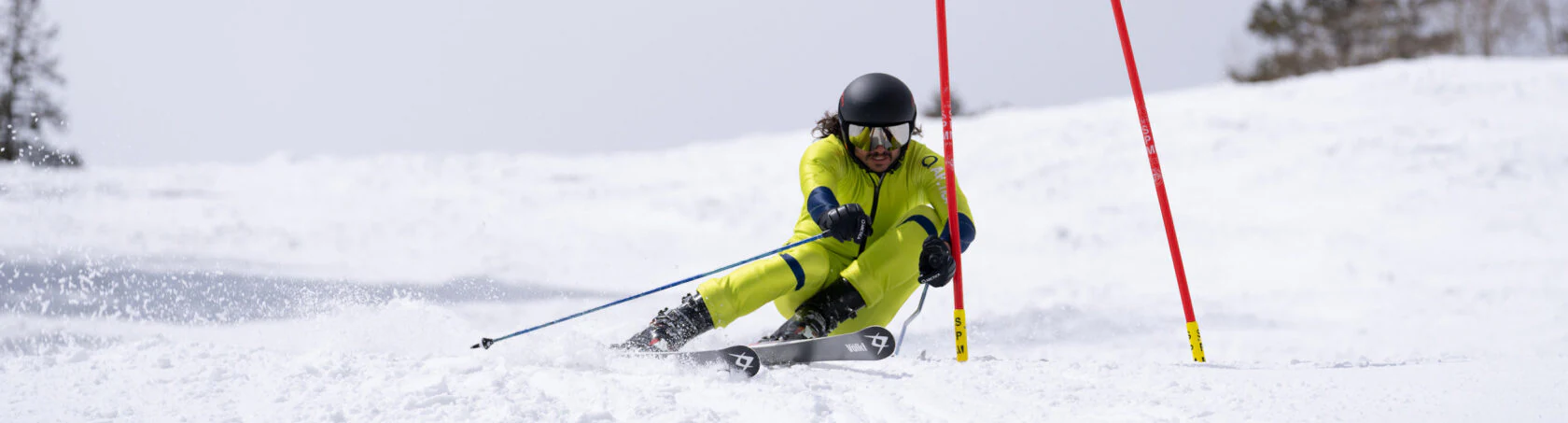 Racer in a yellow Arctica ski race suit carving past red race gates
